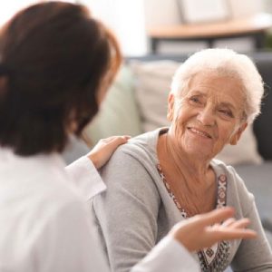 Woman with her hand on a senior woman's shoulder, showing care while talking and smiling.