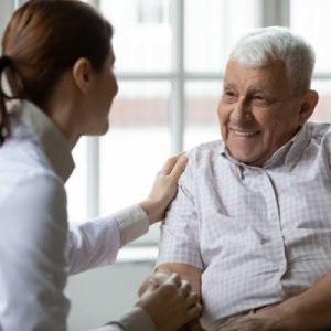 Woman with her hand on a senior man's shoulder, showing care while talking and smiling.