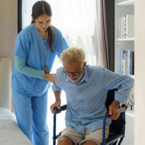 Female healthcare worker helping a senior man up from a chair.