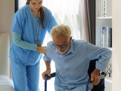 Female healthcare worker helping a senior man up from a chair.